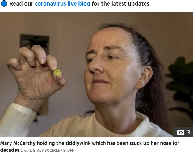 摘出されたプラスチック製の円盤のおもちゃを手に取るメアリーさん（画像は『The Sun　2021年6月28日付「NOSE FOR TROUBLE Woman finds TIDDLYWINK up her nose which has been lodged there for 37 years after taking Covid test」（Credit: STACY SQUIRES / STUFF）』のスクリーンショット）