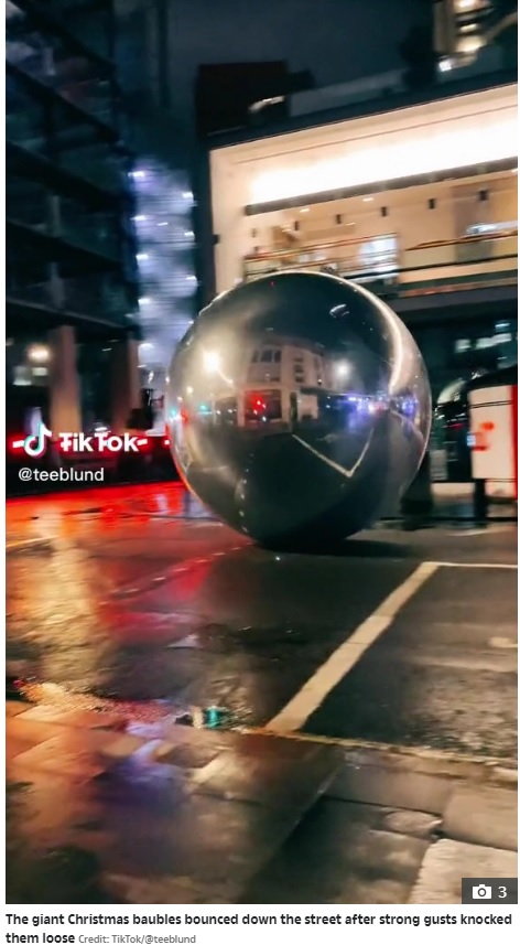 車道を転がる巨大な銀色の球体（画像は『The Sun　2022年11月1日付「YOU BETTER WATCH OUT Moment giant Christmas baubles the size of a bus roll down West End street after high winds blow them down」（Credit: TikTok/＠teeblund）』のスクリーンショット）