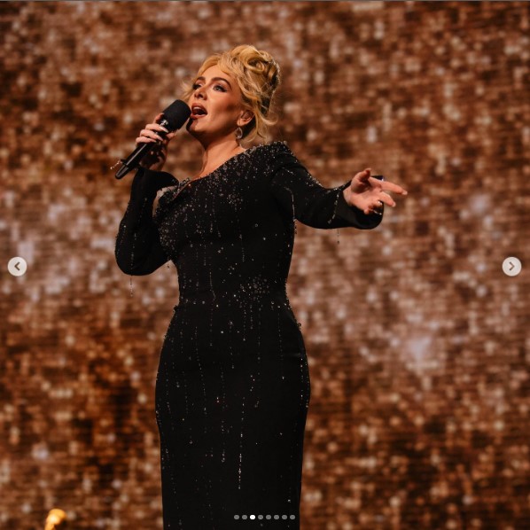 ラスベガスのステージで歌唱するアデル。ブロンドのロングヘアをまとめ、黒いドレスを纏っていた（画像は『Adele　2023年8月26日付Instagram「Weekend 24」』のスクリーンショット）