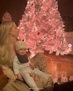 娘ロンドンちゃんの誕生を祝し、ピンクのクリスマスツリーを披露するパリス。膝の上には息子フェニックス君を抱いている（画像は『Paris Hilton　2023年11月25日付Instagram「Celebrating our baby girl London with a pink Christmas!」』のスクリーンショット）