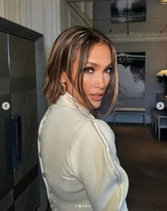 白いタートルネックセーターを着て、振り向くジェニファー・ロペス。耳にはゴールドの大きなイヤリングが輝いている（画像は『Jennifer Lopez　2024年1月22日付Instagram「Couture ＠schiaparelli」』のスクリーンショット）