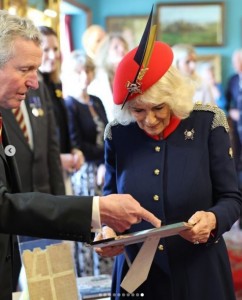 かつて連隊に所属した、生前の父親の写真を見せてもらうカミラ王妃。赤いベレー帽にはスカルとクロスボーンの帽章と羽根が付いている（『The Royal Family　Instagram「The Queen has paid her first visit to The Royal Lancers, since becoming their Colonel-in-Chief, in North Yorkshire.」』より）