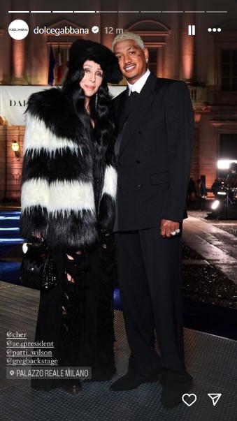 約40歳年下の恋人アレクサンダーと仲良く寄り添うシェール。全身黒のファッションにファーのコートを合わせている（『Dolce＆Gabbana　Instagram』より）