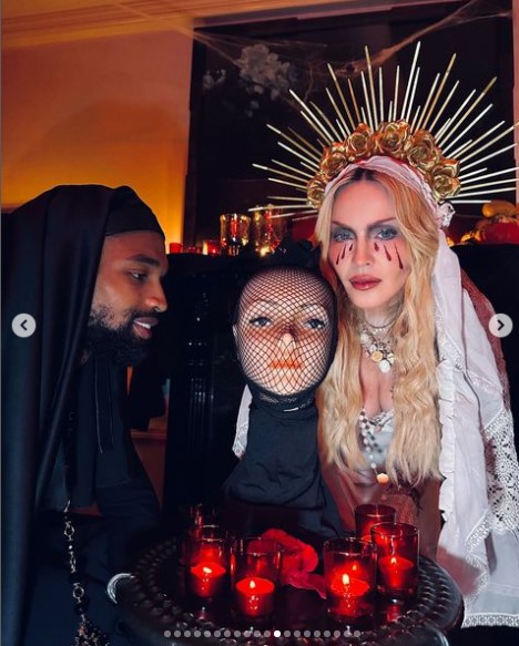 キャンドルを並べたテーブルの前に座るマドンナとアキーム。マドンナはマネキンの顔を持っていた（『Madonna　Instagram「For Halloween, I was the Crying Madonna」』より）